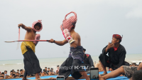 MERAWAT: Dua petarung saling adu ketangkasan dalam tradisi Ojung di atas panggung terbuka, berlatar Pantai Badur, Kecamatan Batuputih, Sumenep, Sabtu (17/5/2025).(K-TV/Taufiq Hidayat)