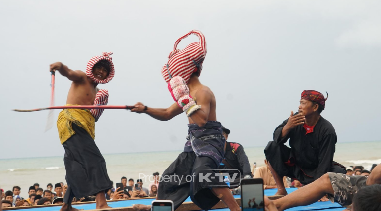 MERAWAT: Dua petarung saling adu ketangkasan dalam tradisi Ojung di atas panggung terbuka, berlatar Pantai Badur, Kecamatan Batuputih, Sumenep, Sabtu (17/5/2025).(K-TV/Taufiq Hidayat)